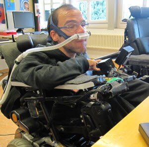 Foto einer Person im Rollstuhl, die eine Joystick-Maus bedient.